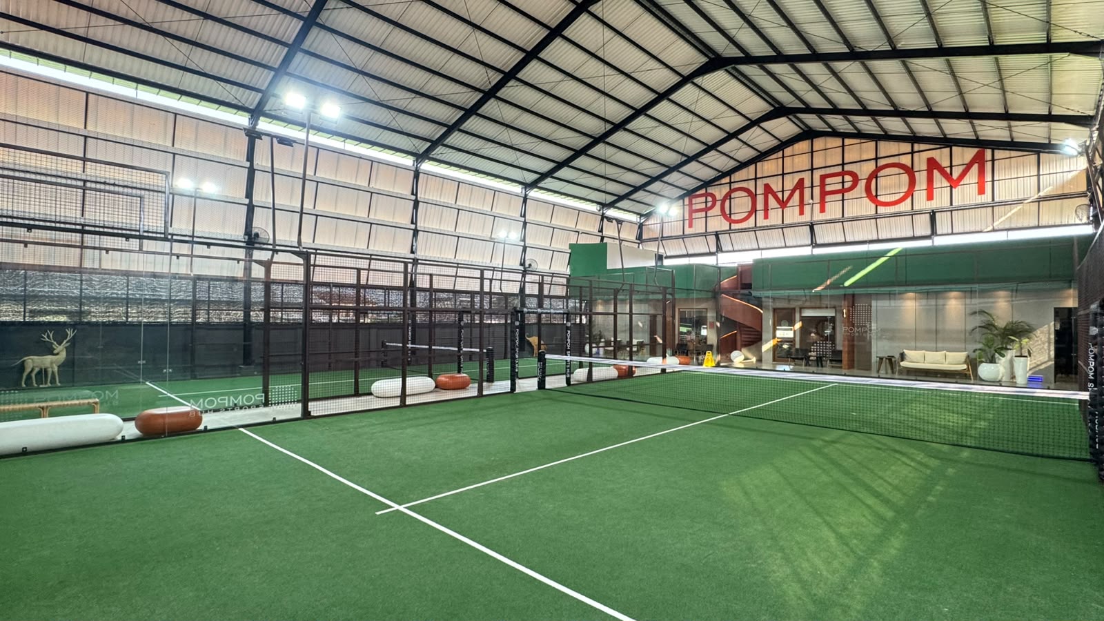 Full size double padel court at PomPom Sports Hub with vibrant Wimbledon green surface and dark brown iron pillars