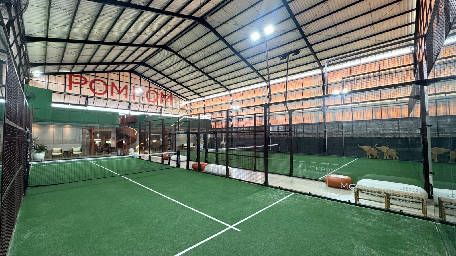 Half size single padel court at PomPom Sports Hub featuring green surface and elegant dark brown iron pillars
